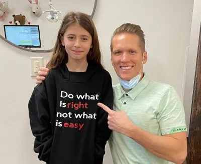 Child in black sweatshirt with motivational quote alongside smiling orthodontist in green shirt, showcasing friendly patient interaction at Garlock Orthodontics.